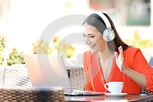 Happy woman having a video call with a laptop in a bar