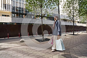 Happy woman in headscarf and jacket walking with shopping bags