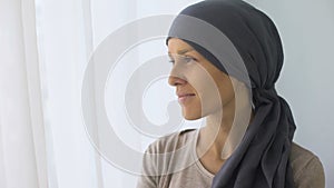 Happy woman in headscarf looking in window, recovery after cancer treatment