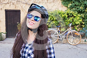 Happy woman with helmet and sunglasses posing backgound bicycle and street