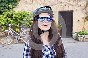 Happy woman with helmet and sunglasses posing backgound bicycle and street