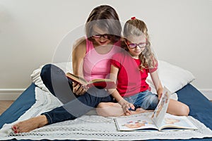 Happy woman with her daughter child, reading together a book a