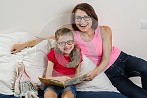 Happy woman with her daughter child, reading together a book a