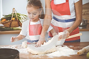 Happy woman and her daughter are kneading the dough and baking cookies for a delicious family feasting. Christmas, New