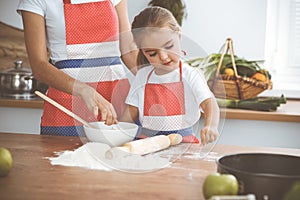 Happy woman and her daughter are kneading the dough and baking cookies for a delicious family feasting. Christmas, New