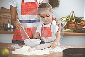 Happy woman and her daughter are kneading the dough and baking cookies for a delicious family feasting. Christmas, New