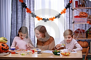 Happy woman with her daughter and son getting ready for Halloween. The family sits at the table, the mother helps the