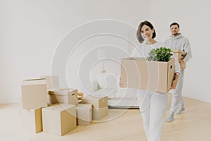 Happy woman and her husband carry boxes with personal belongings, being busy during relocation in other place for living, enter