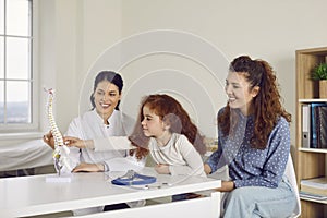 Happy woman and her little child looking at human spine model at doctor's office