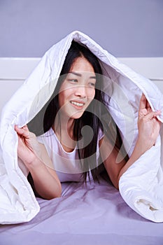 Happy woman hiding under blanket on bed in bedroom