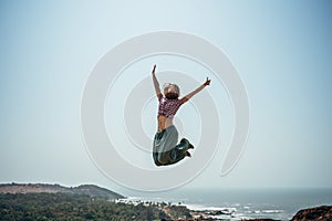 Happy woman high jumping of joy on beach in a casual wear