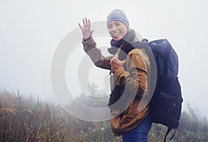 Happy woman, hiking and portrait in nature with wave and greeting for morning adventure in mountain. Healthy person