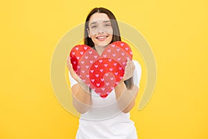 Happy woman hold red heart. Beautiful female model posing on isolated yellow background. Cheerful positive cute pretty