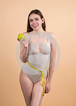 Happy woman holding apple wrapped with measuring tape on waist. Weight loss concept. Dieting and waist exercise. Woman