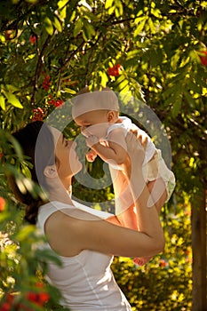 Happy woman holding in arm a baby in a garden. Happy family.