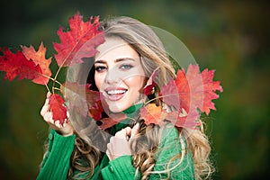 Happy woman holding autumn leafs on face in fall nature. Portrait of young woman with autumn maple leaves outdoor