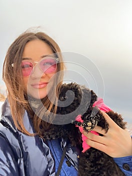 Happy woman holding black puppy outdoors. Female person walking with toy poodle dog in winter. Korean girl with funny