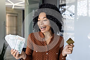 Happy woman holding cash and credit card in office