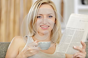 happy woman holding coffee while reading newspaper