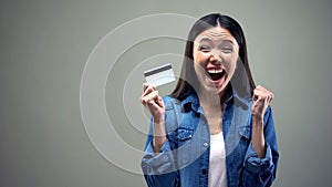 Happy woman holding credit card in hands, cash back services, grey background