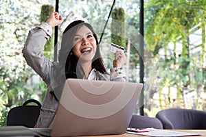 Happy woman holding a credit card and using laptop computer for
