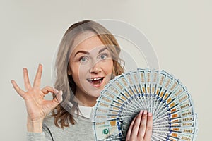 Happy woman holding fan of us dollars money showing ok sign on white background. Happy girl hand okay symbol