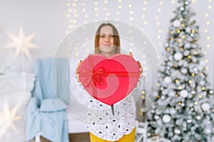 Happy woman holding a gift red box in christmas decoration at home.
