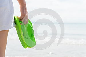 Happy woman holding green flip flop on sandy beach for summer