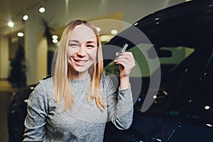 Happy woman holding keys to her new car at the dealership.