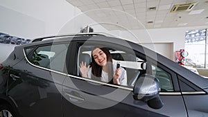 Happy woman holding keys to her new car at the dealership. Right hand drive car