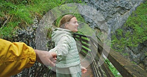 Happy woman holding man hand looking at him and hiking along narrow path in mountains. Follow me gesture. Couple