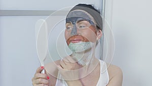Happy woman holding mirror and examining face mask