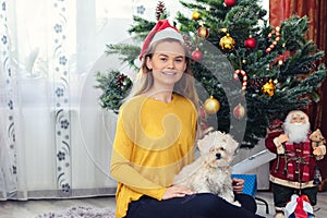 Happy woman holding puppy dog Christmas gift sitting on the floor near Christmas tree