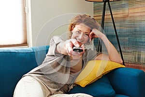 Happy woman holding remote control lying on cozy couch