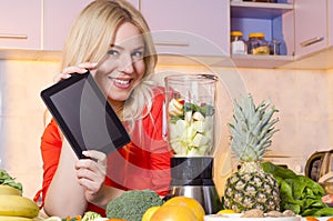 Happy woman holding tablet next to a juicer full of fruit