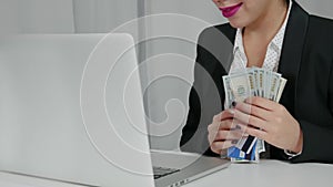 Happy woman holding US dollars and credit cards near her laptop.