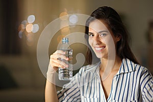 Happy woman holding water bottle at home in the night