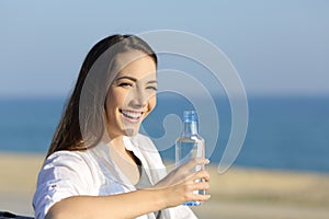 Happy woman holding a water bottle and looking at you outdoors