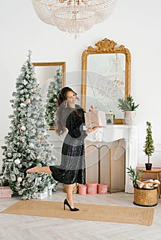 A happy woman holds a Christmas gift in her hands and opens it at the Christmas tree