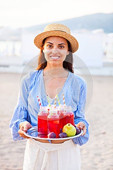 Happy woman holds a dish with a drinks red juice at sunset. Picnic theme on the beach