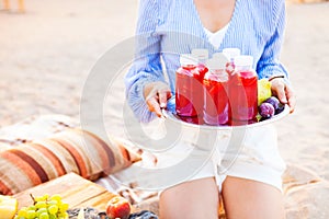 Happy woman holds a dish with a drinks red juice at sunset. Picnic theme on the beach