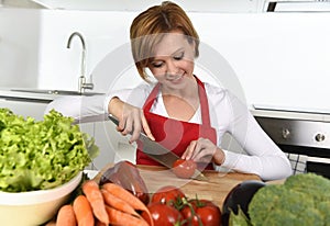 Happy woman at home kitchen preparing vegetable salad with lettuce carrots and slicing tomato