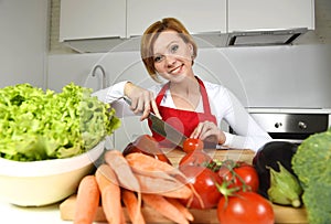 Happy woman at home kitchen preparing vegetable salad with lettuce carrots and slicing tomato