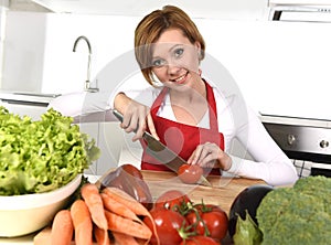 Happy woman at home kitchen preparing vegetable salad with lettuce carrots and slicing tomato