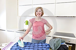 happy woman or housewife ironing shirt at home kitchen using iron and board smiling cheerful