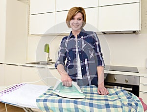 happy woman or housewife ironing shirt at home kitchen using iron and board smiling cheerful