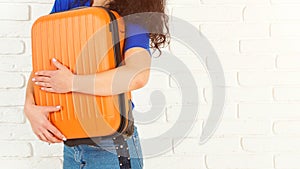 Happy woman hugging her orange suitcase. Isolated on white, copy space. Casual girl is ready to travel. Stylish woman dreaming