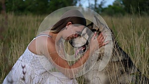 Happy woman hugging and kiss alaskan malamute dog in summer field