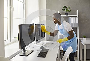 Happy woman from janitorial cleaning service wiping computer screens in modern office