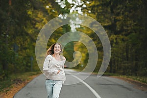 Happy woman in jeans is runnning on asphalt road in autumn forest